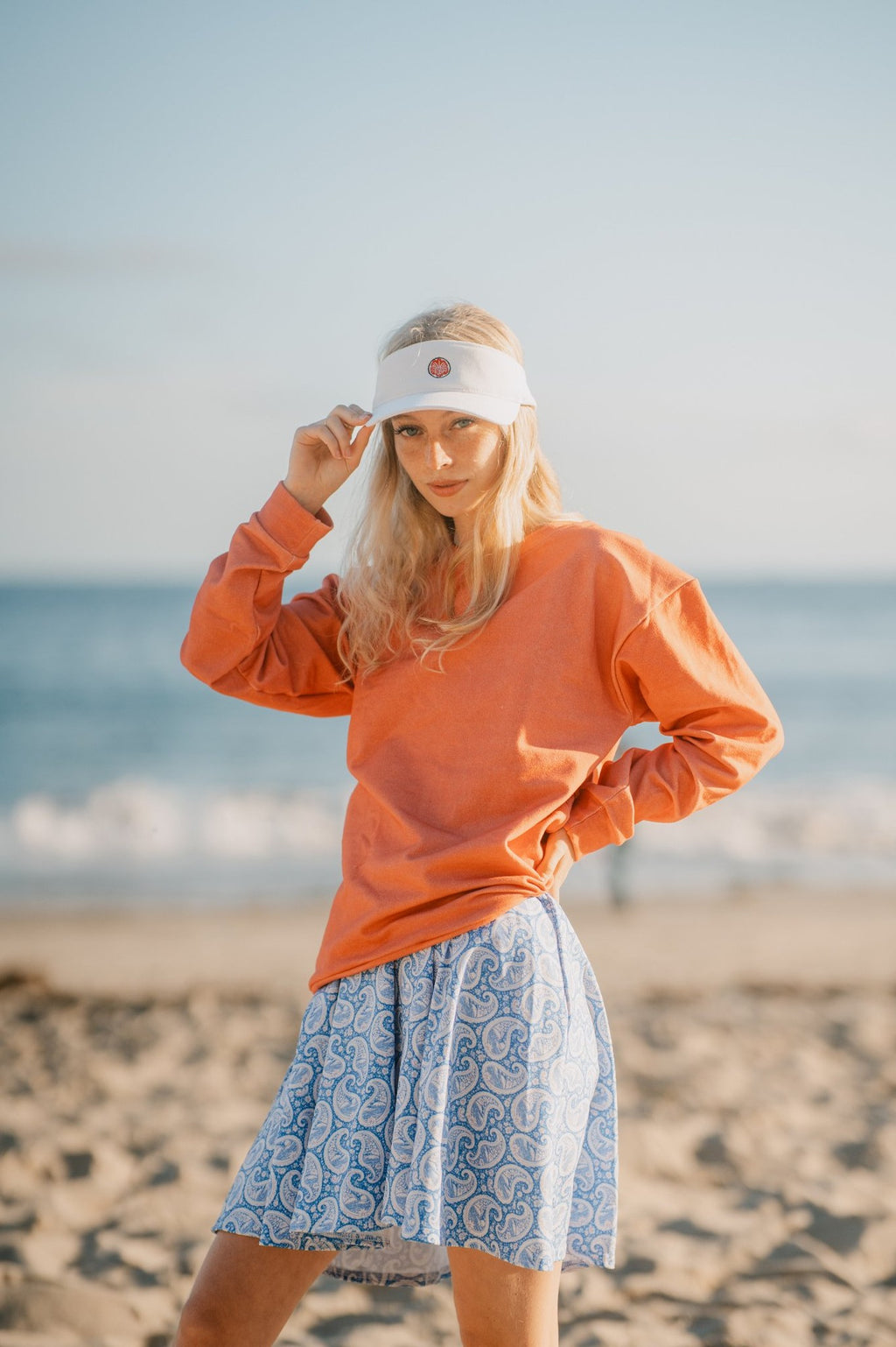 Woman wearing an orange sweatshirt and white visor on a beach