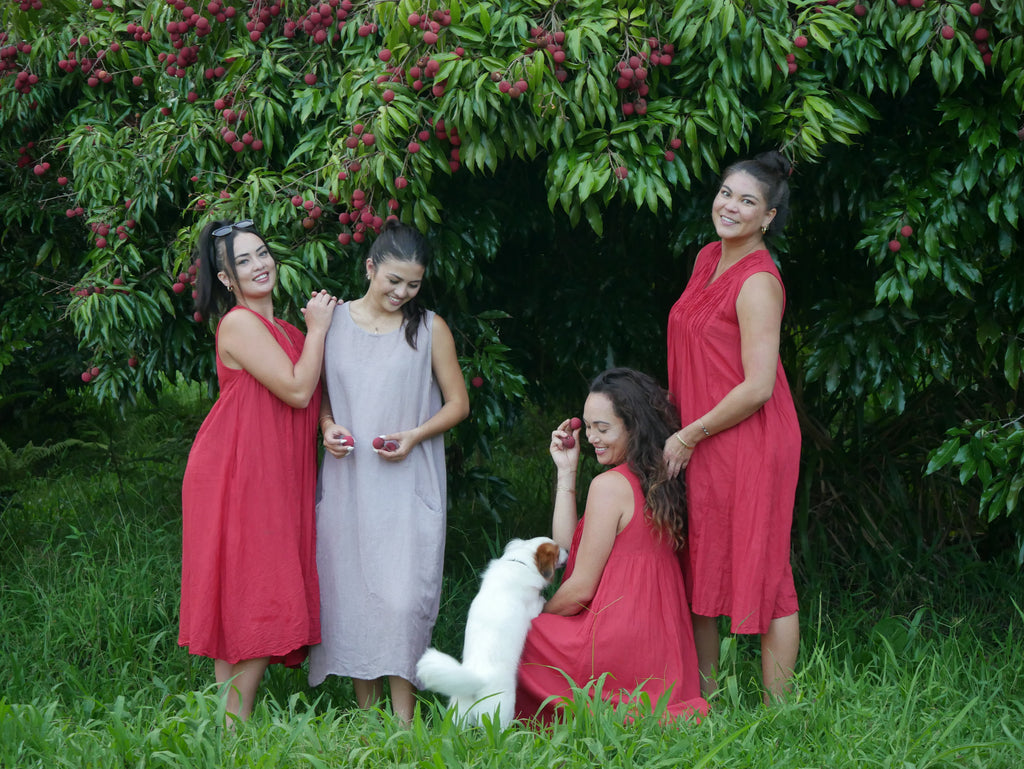 Model in a soft Kahoʻolawe-toned sleeveless linen midi dress with round neckline and pockets, wearing lei, photographed on a Hilo farm.