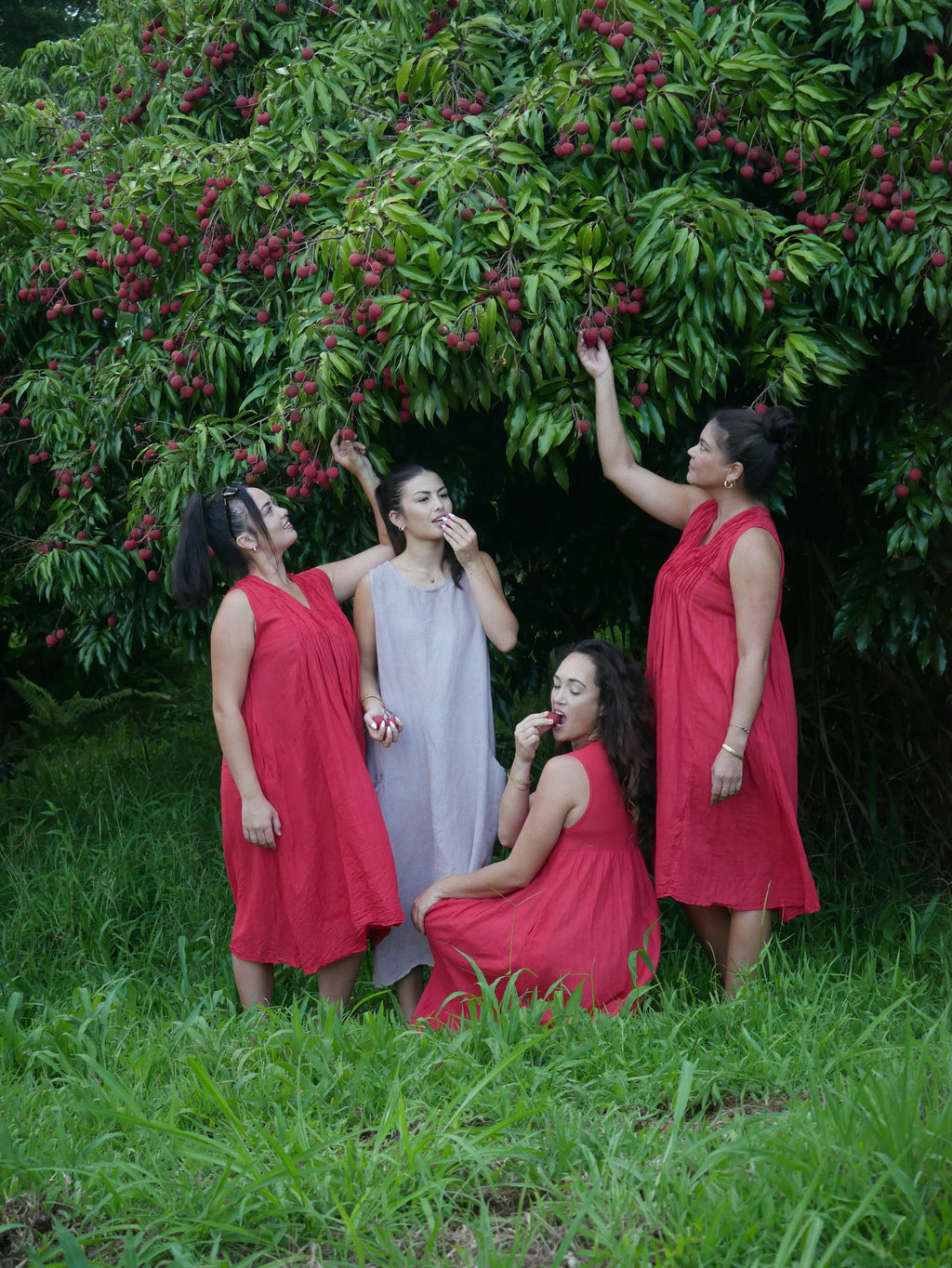 Model in a deep lychee-red cotton A-line dress with V-neckline and pockets, photographed on a Hilo farm.