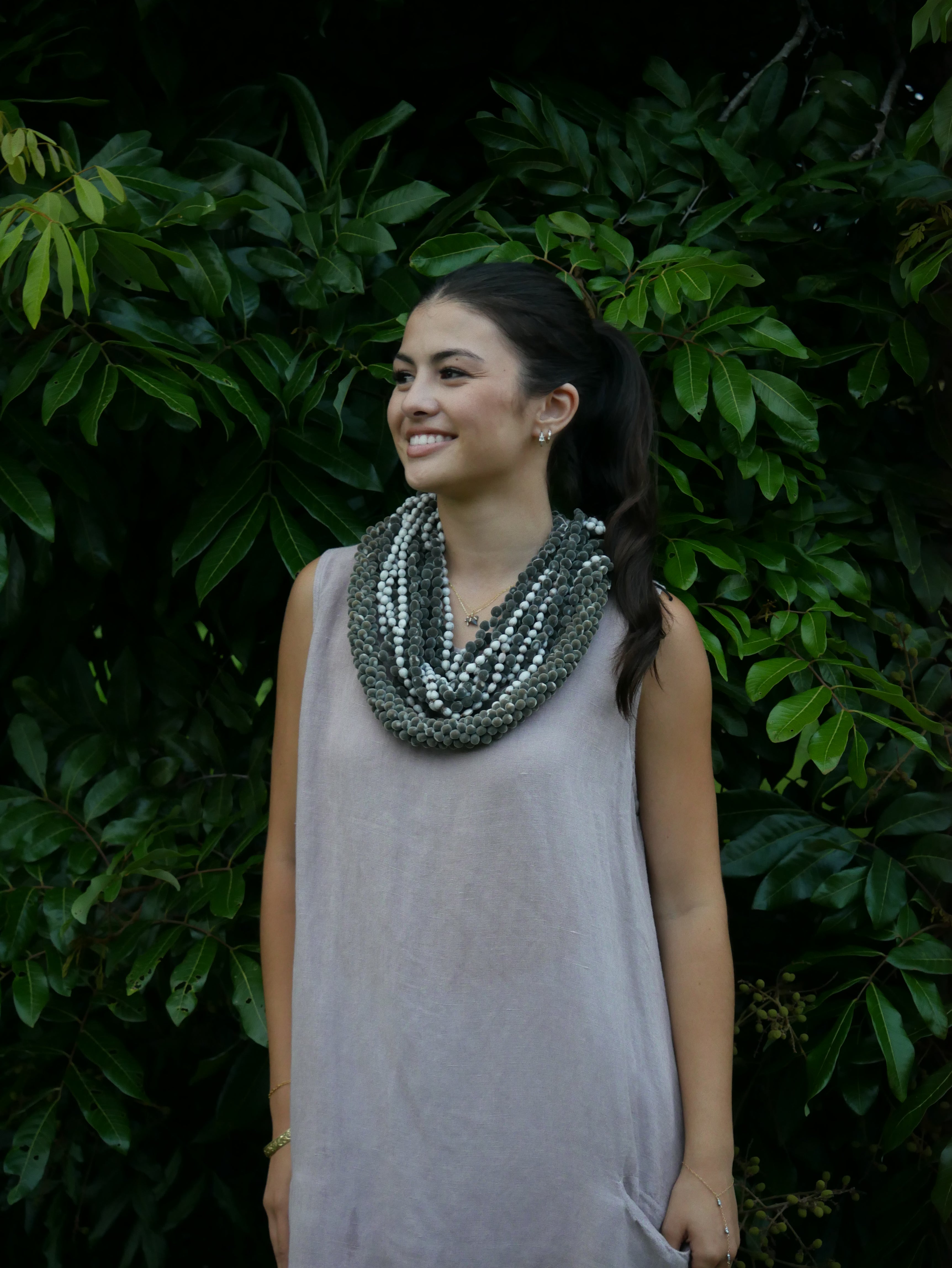 Model in a soft Kahoʻolawe-toned sleeveless linen midi dress with round neckline and pockets, wearing lei, photographed on a Hilo farm.